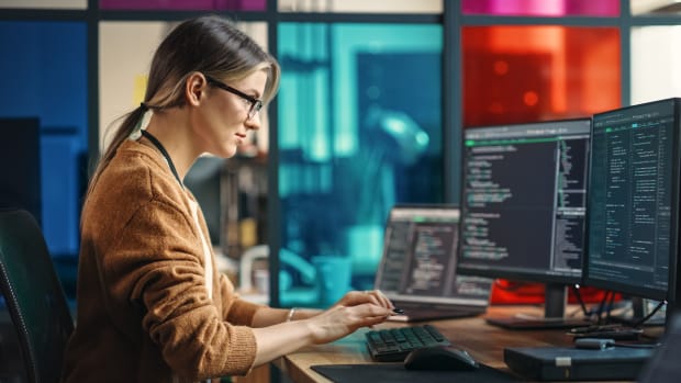 An IT employee works at a desktop station with three monitors.